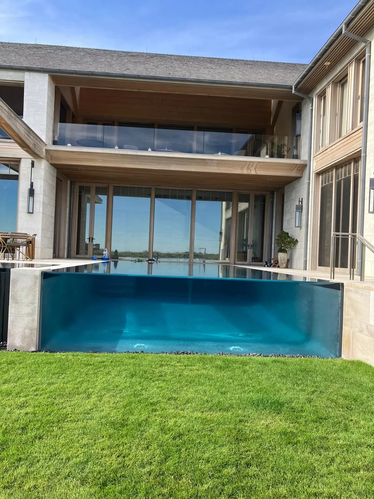 A private pool with a glass wall, in front of a house. Nobody in frame.